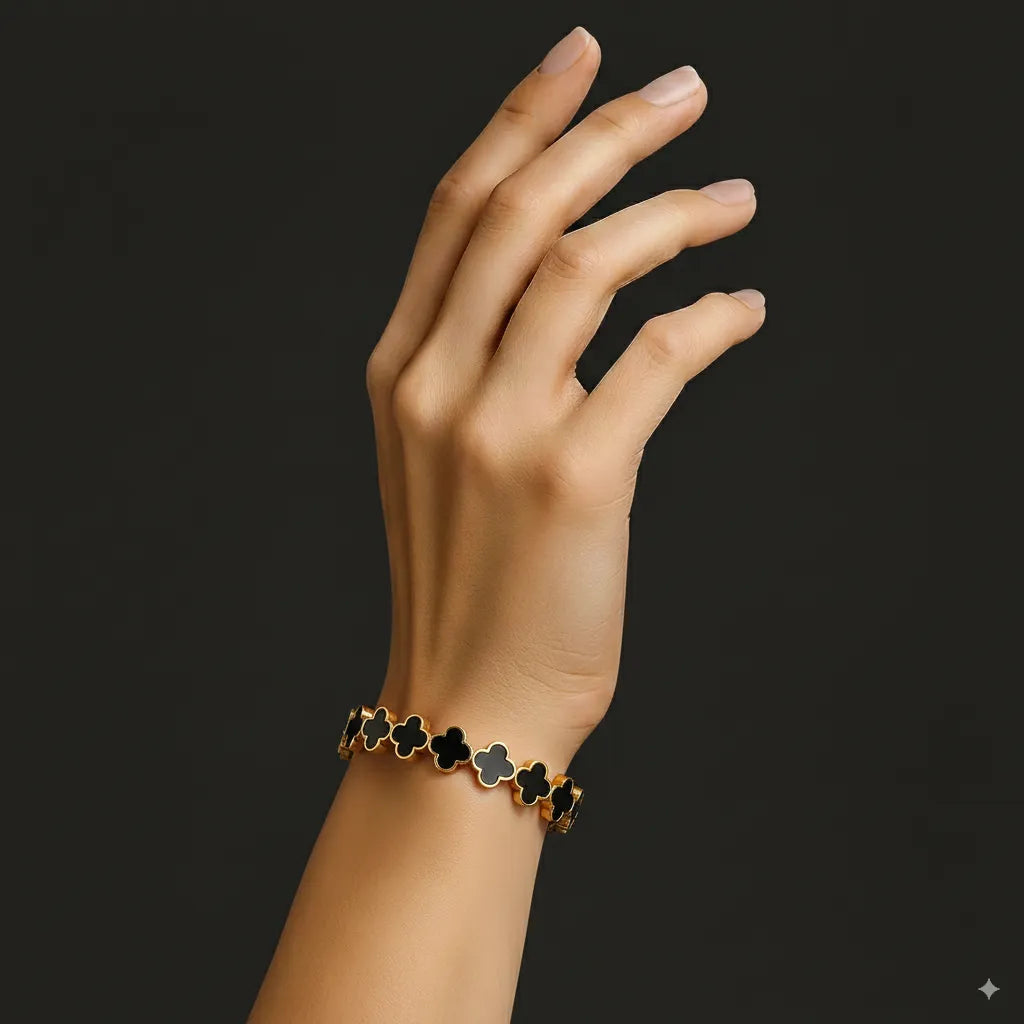 Hand wearing a bracelet with black clover-shaped charms on a dark background